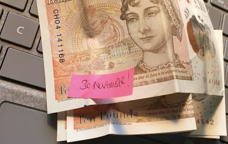 Photo showing three ten pound notes on a grey keyboard with the words '30 November' written on a pink post it stuck on top of the top note